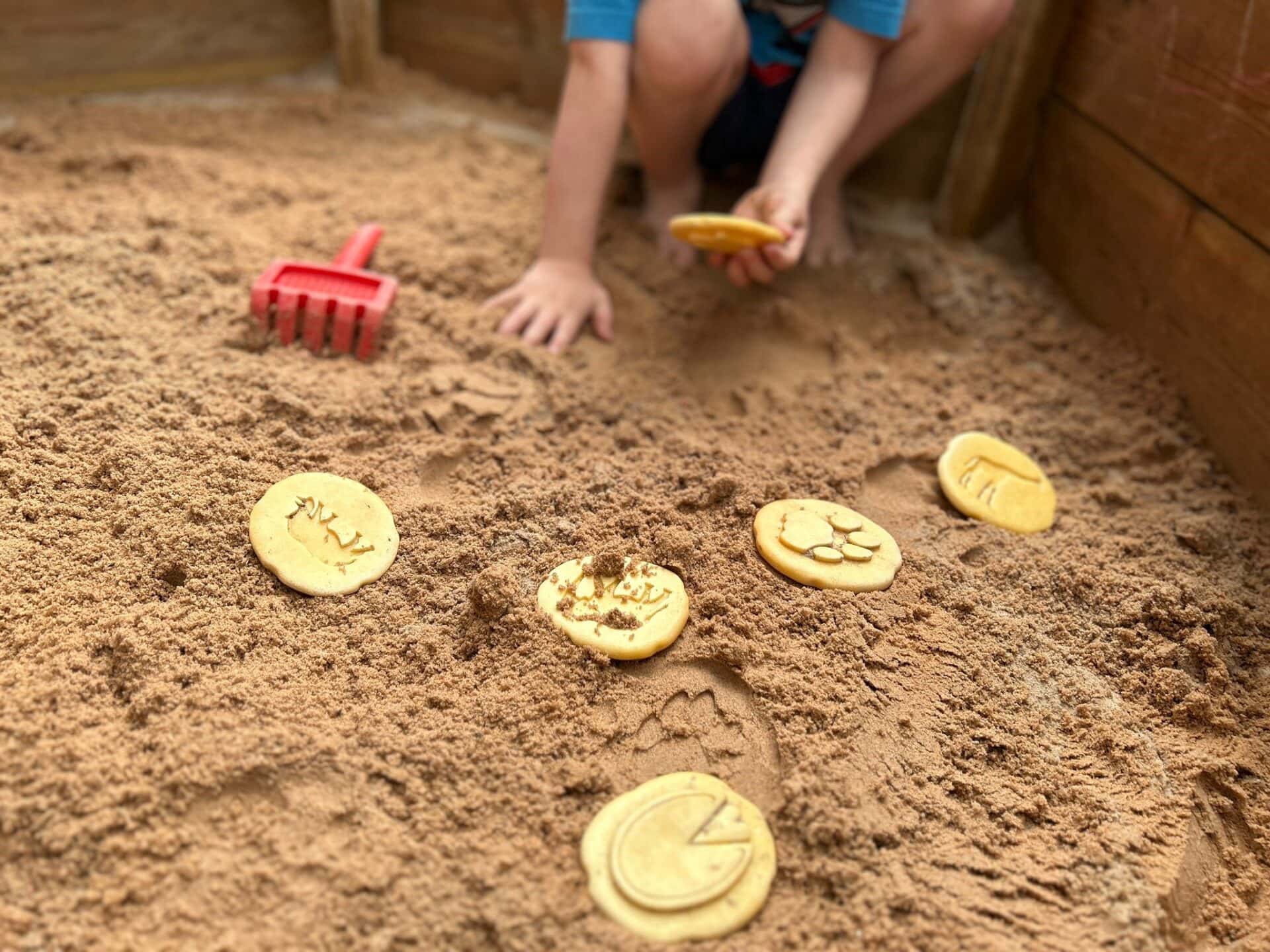 A child playing in a sand pit with coins.